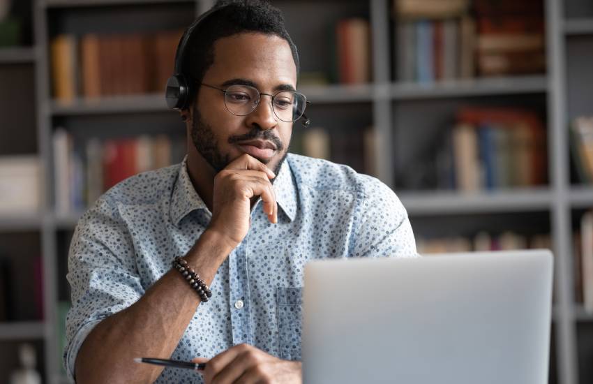 Focused man wearing headphones with microphone looking at laptop screen.