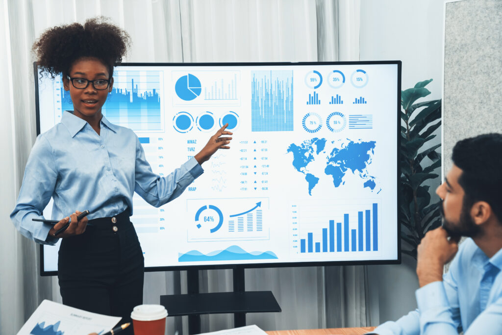 Young businesswoman presenting data analysis dashboard on TV to businessman colleague.