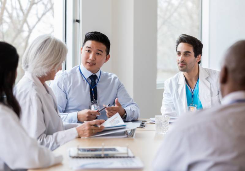 Group meeting of diverse medical professionals sitting at a table reviewing study results.