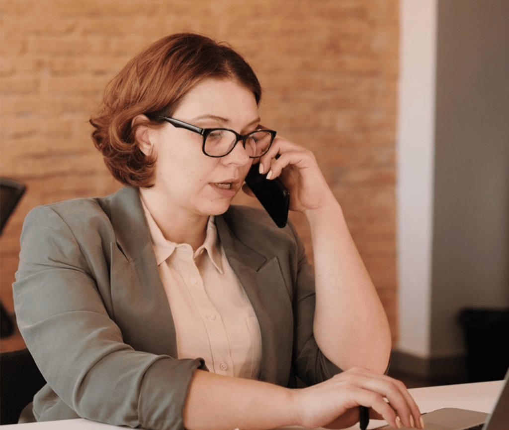 Business woman talking on her phone while sitting at her desk and working on her laptop.