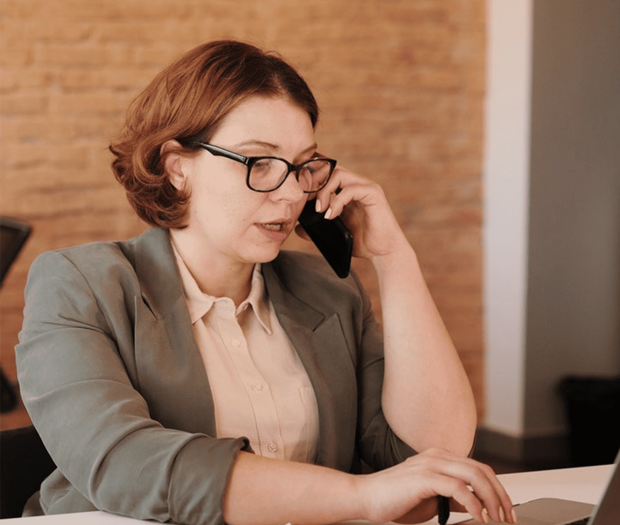 Business woman talking on her phone while sitting at her desk and working on her laptop.