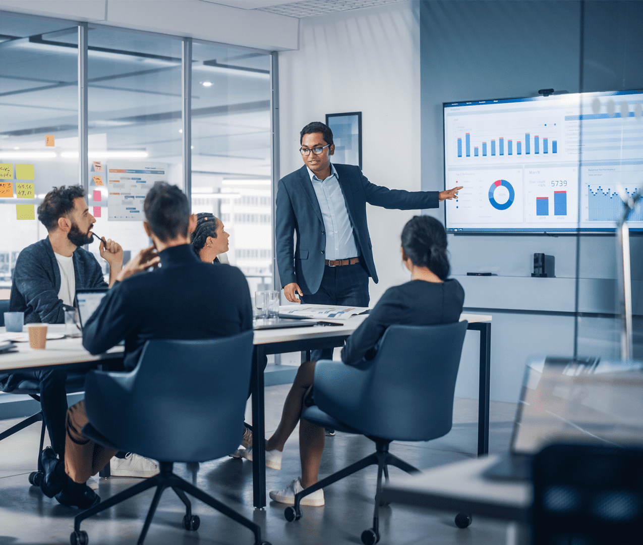Business meeting with man presenting results on a metrics dashboard to his colleagues sitting at a boardroom table and listening.