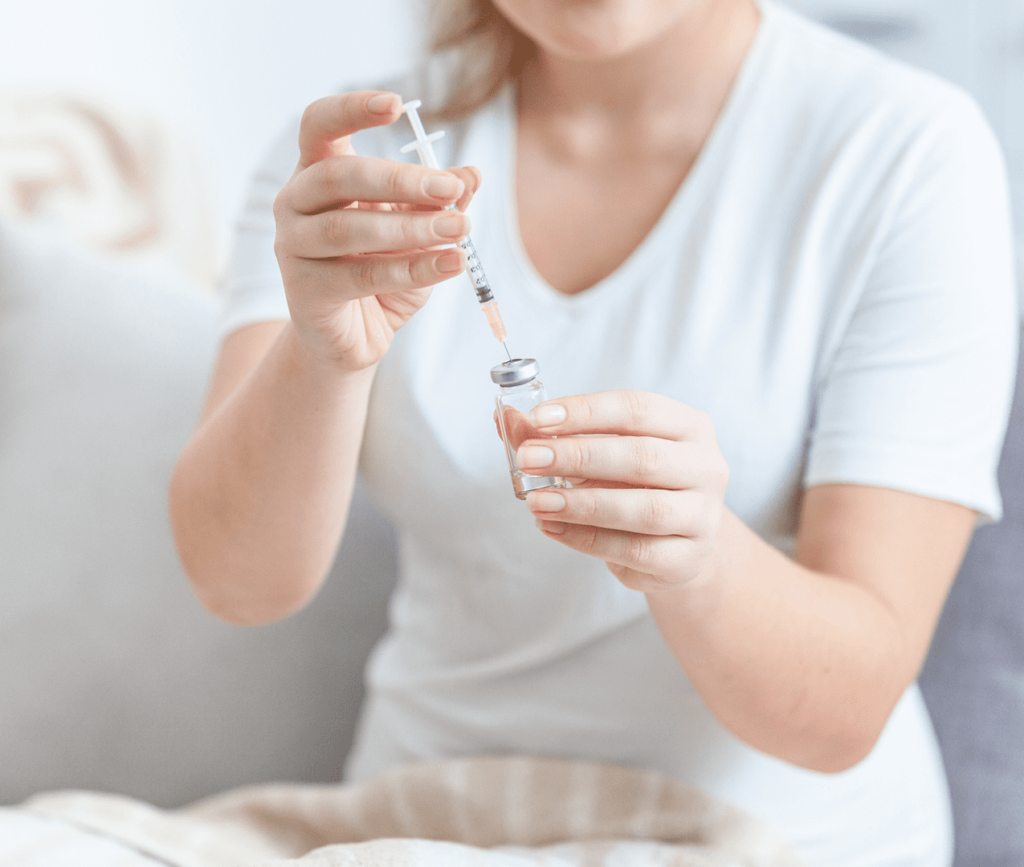 Closeup action photo of an unknown female pushing a syringe into a held vial without a label.