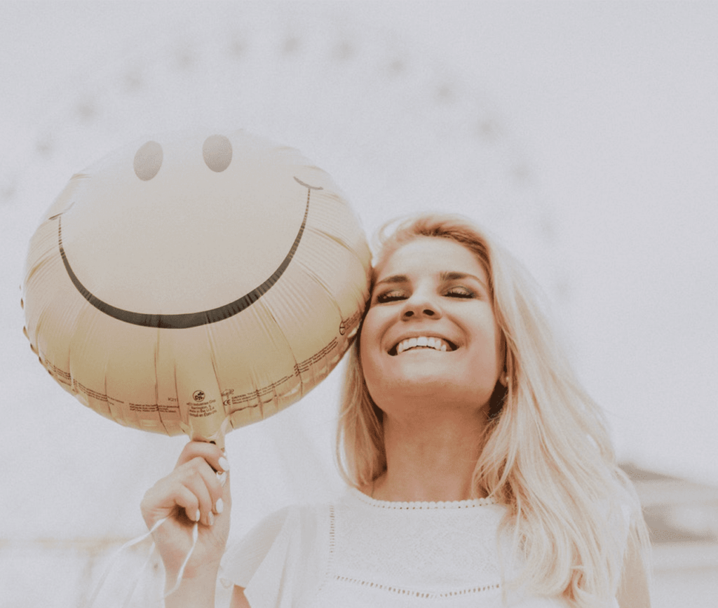 Smiling woman holding a balloon with a happy face imprint.