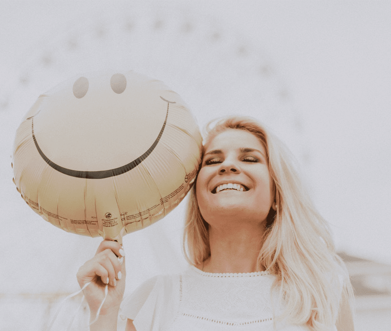 Smiling woman holding a balloon with a happy face imprint.