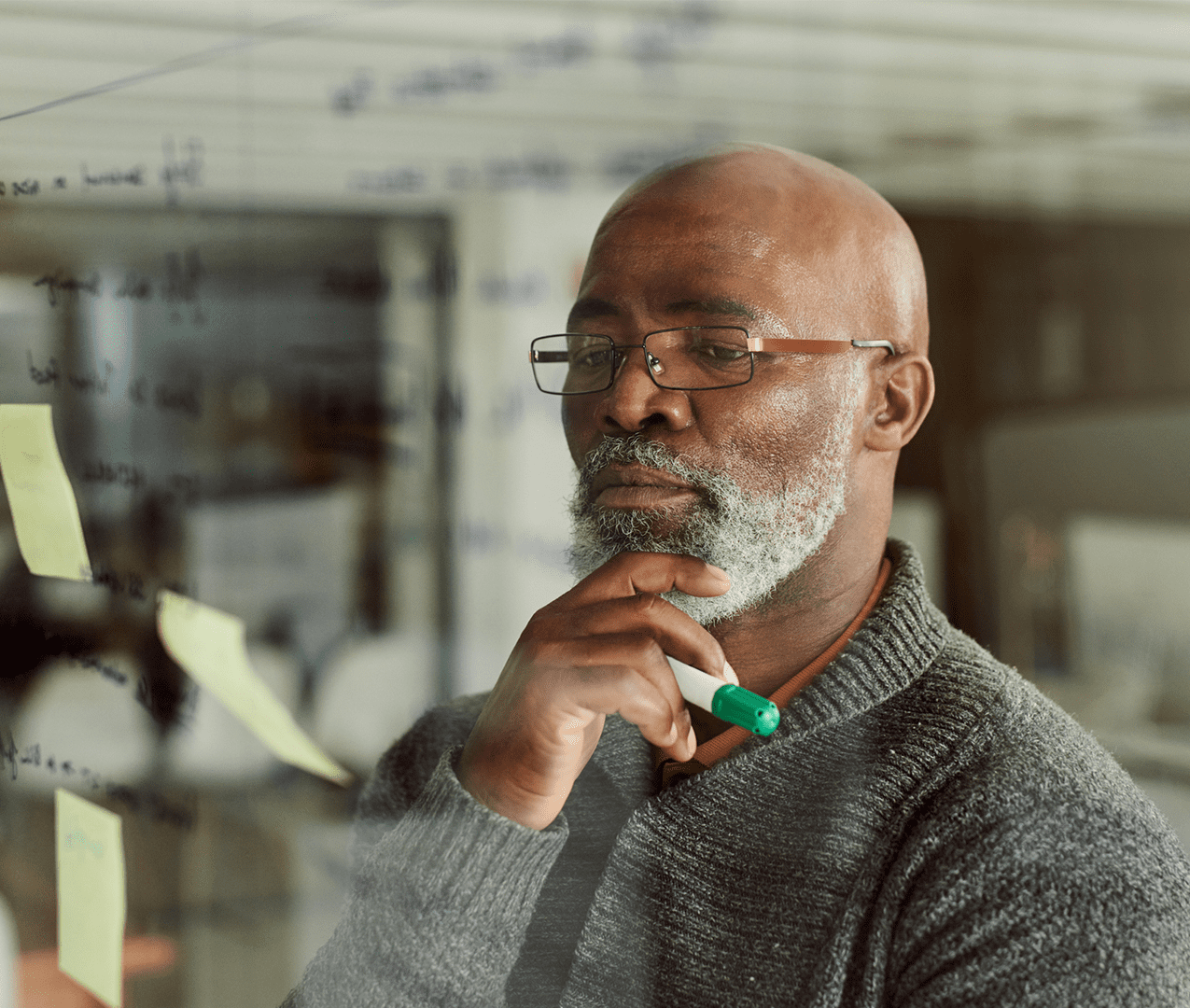 Older professional looks at a clear board with sticky notes and reviews their contents.